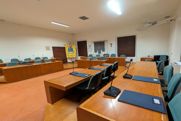 Sala consiliare, con scrivanie, microfoni e cartelline